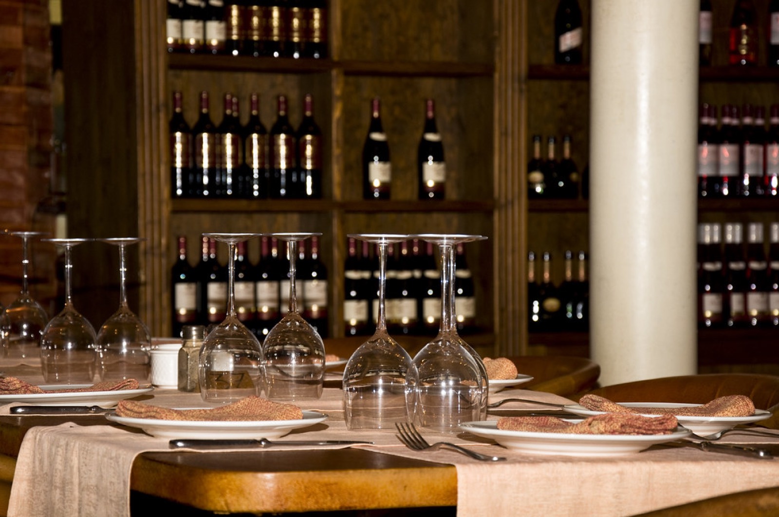 A candlelit restaurant table set with wine glasses in front of a wall of wine bottles
